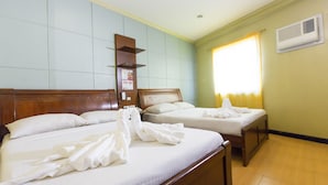 Ein Hotelzimmer mit zwei Betten, einem hölzernen Kopfteil, einer Wand-Klimaanlage und einem Fenster mit Vorhängen.