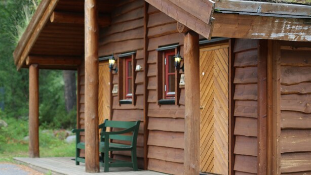 A wooden cabin with a porch, a green bench, and a door with a window. - Saltdal Turistsenter - Campground (Saltdal)