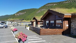 A rustic lodge with stone walls and wooden beams, a parking area with cars, and a mountain backdrop. - Saltdal Turistsenter - Campground (Saltdal)