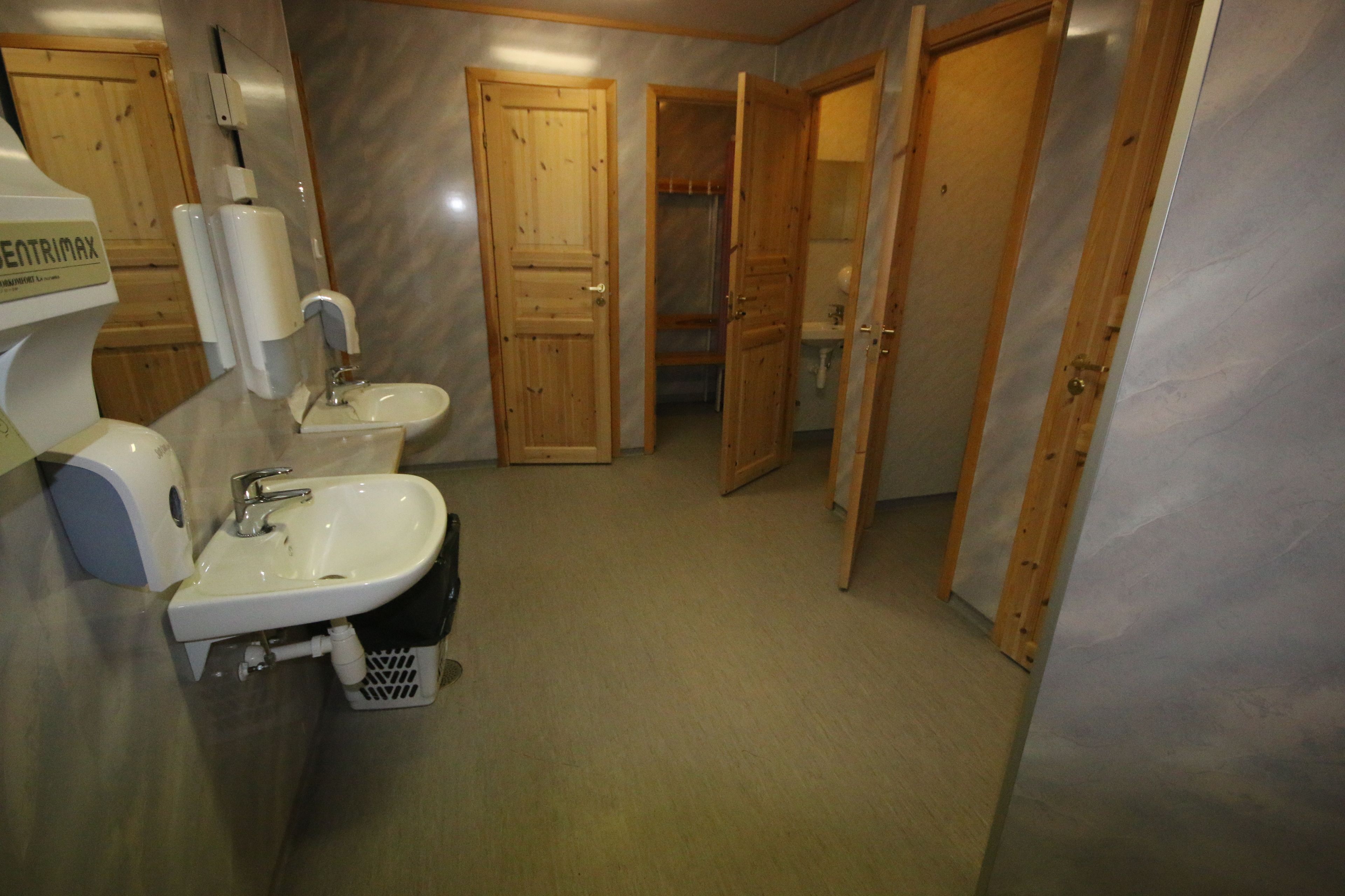 A bathroom with a sink, a toilet, and a shower area. There are wooden doors and a sign that reads "ENTRIX".