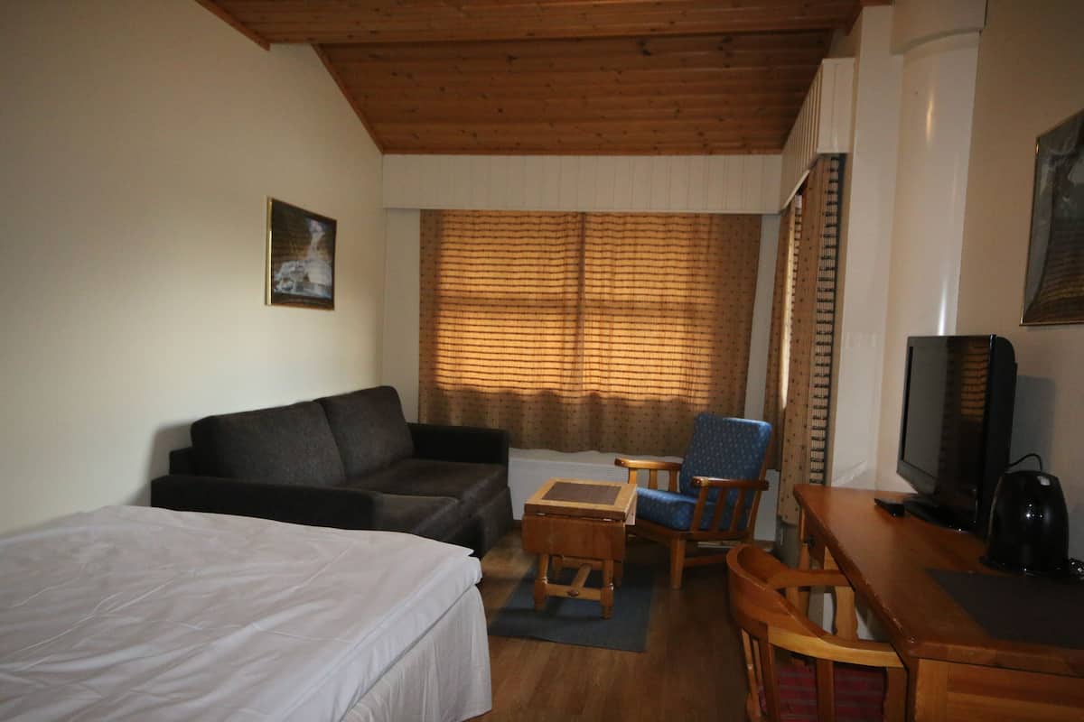 Una habitación con una cama, un sofá, una mesita, una silla, un televisor y una ventana con cortinas.