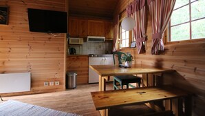 A wooden cabin interior with a kitchen area, a dining table, and a television mounted on the wall. - Saltdal Turistsenter - Campground (Saltdal)
