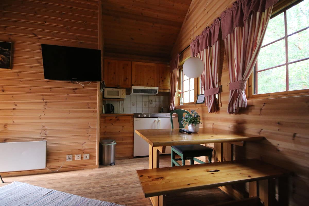 Interior de una cabaña de madera con una cocina, una mesa de comedor y un televisor montado en la pared.