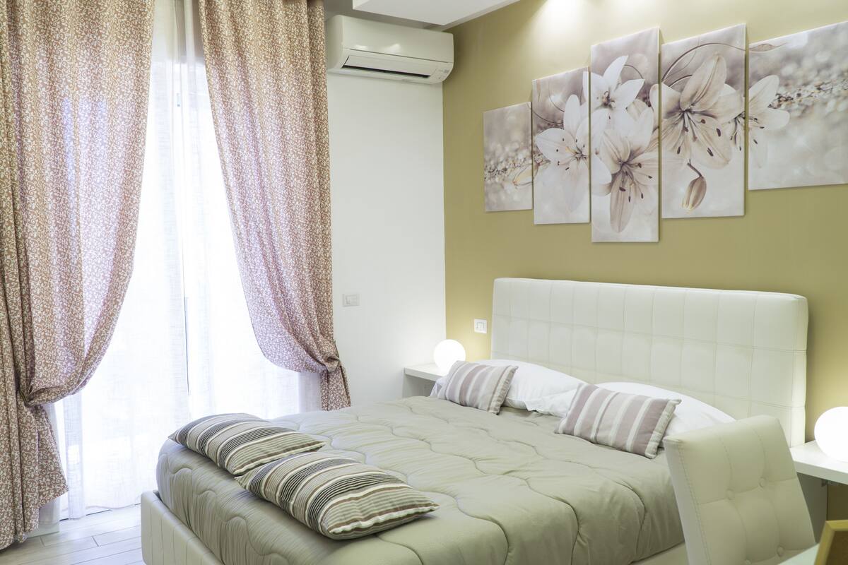 Un dormitorio con una cama grande, una mesita de noche y un aire acondicionado de pared.