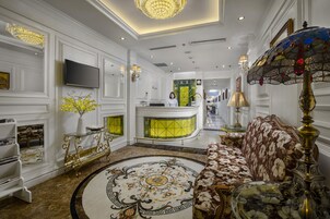 A luxurious lobby with a reception desk, a sofa, a chandelier, and a decorative floor pattern.