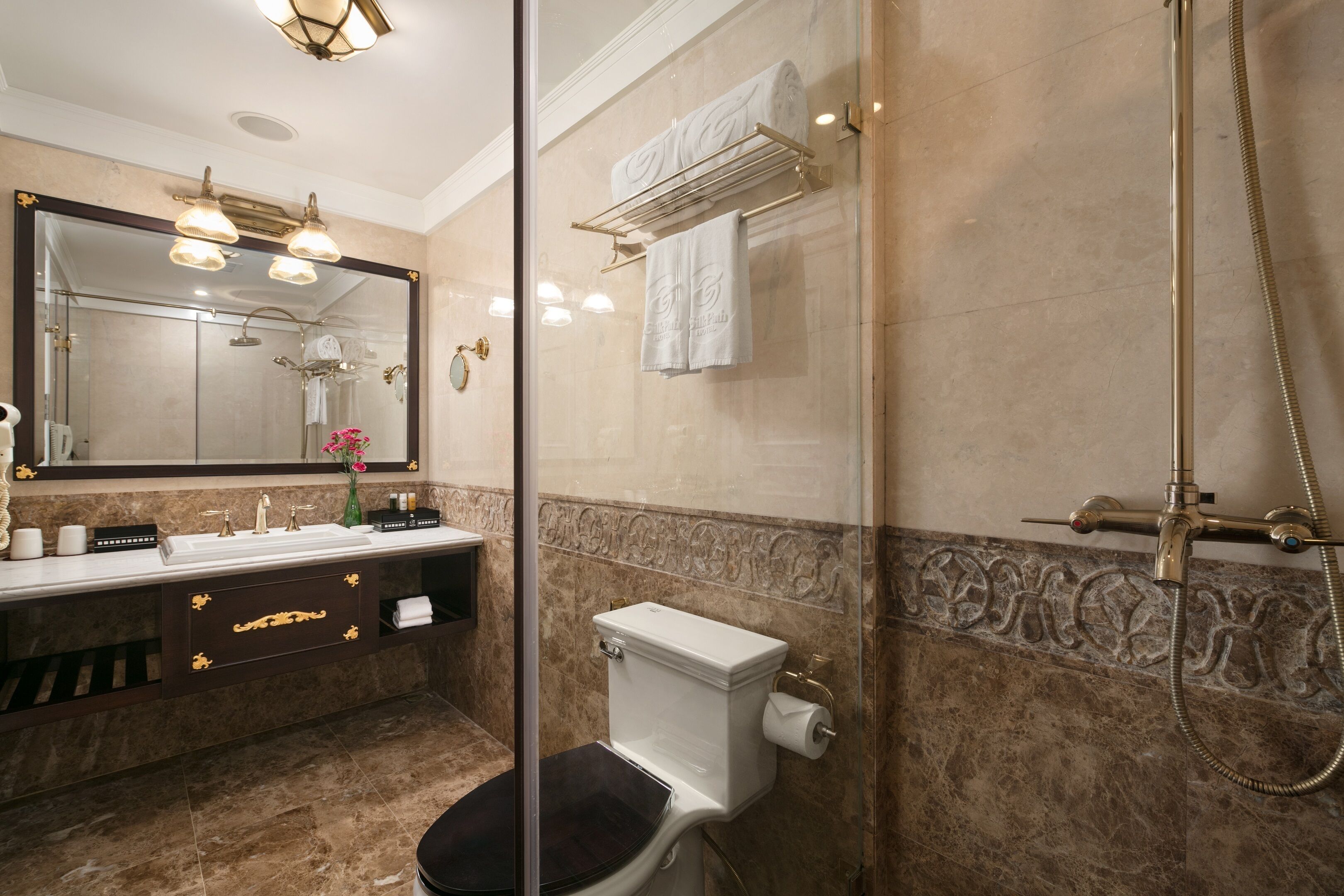 Un baño con lavamanos de mármol, inodoro, cabina de ducha de vidrio y tocador con espejo.