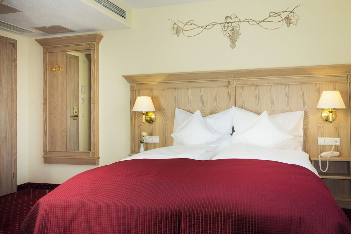 A hotel room with a large bed, two bedside lamps, a mirror, and a wall-mounted light fixture.
