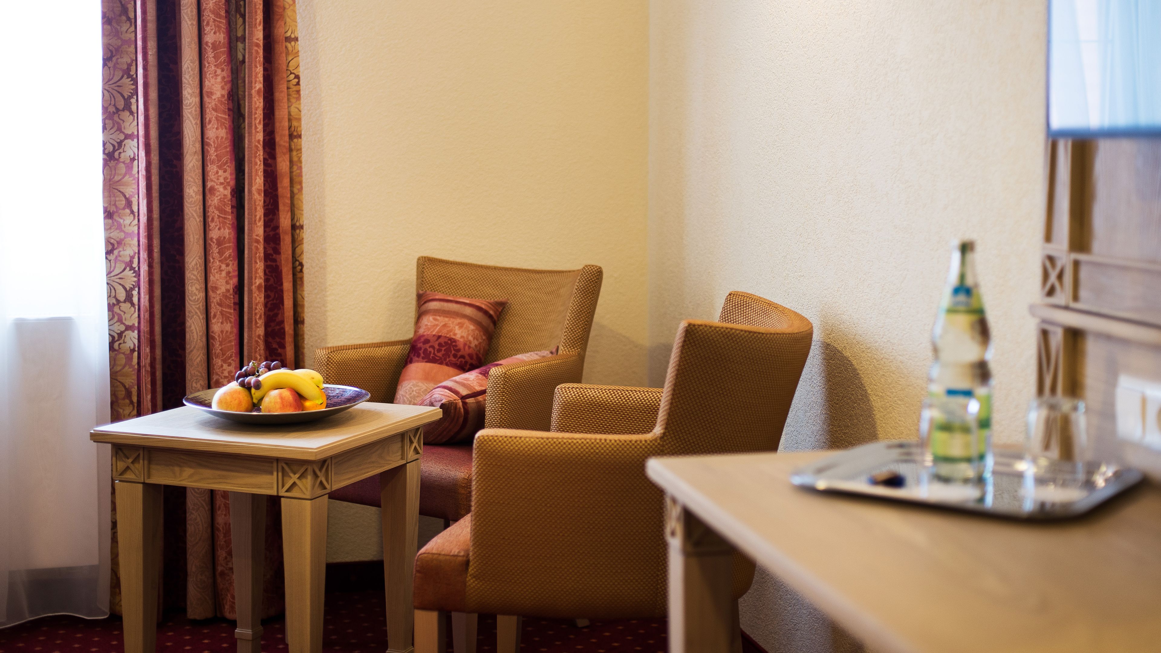 Een hotelkamer met een houten tafel, een stoel, een bank en een kleine tafel met een fruitschaal.