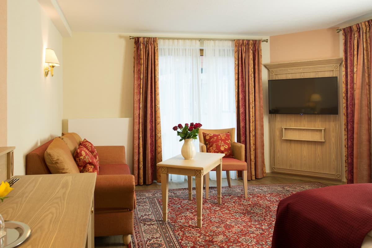 A hotel room with a sofa, a small table with a vase of flowers, a television, and a wooden cabinet.