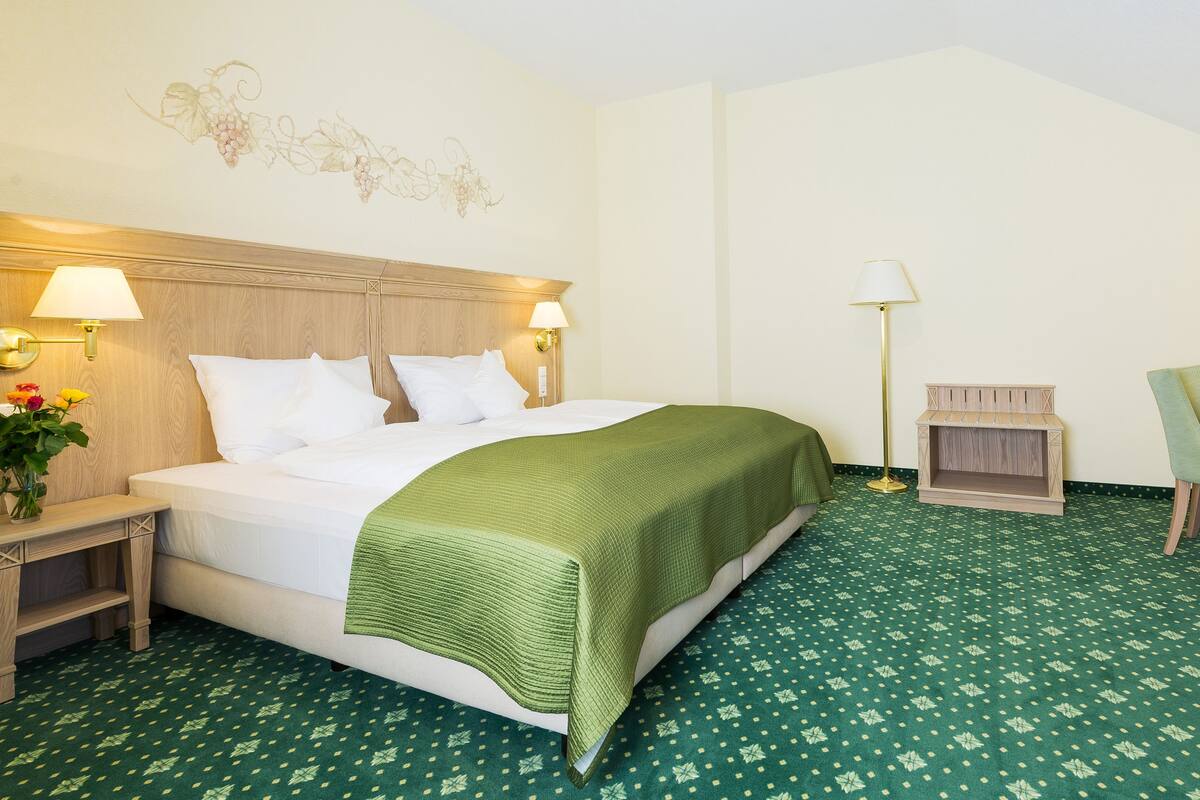 A hotel room with a bed, bedside lamps, a desk with a chair, and a patterned carpet.