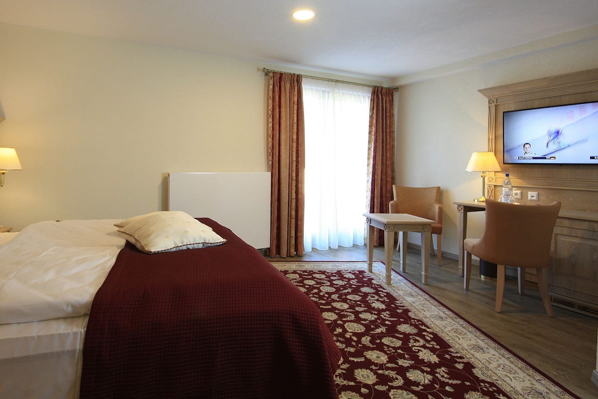 A hotel room with a bed, a desk, a chair, a television, and a window with curtains.