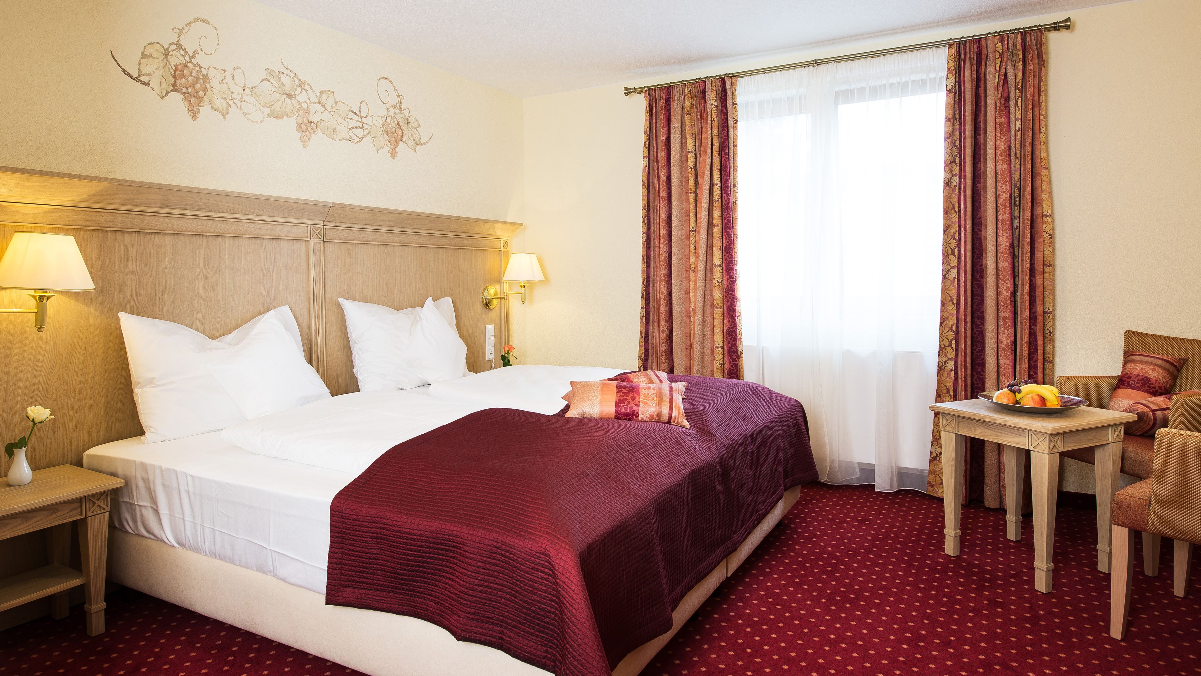 A hotel room with a large bed, two bedside lamps, a small table with fruit, and a chair.