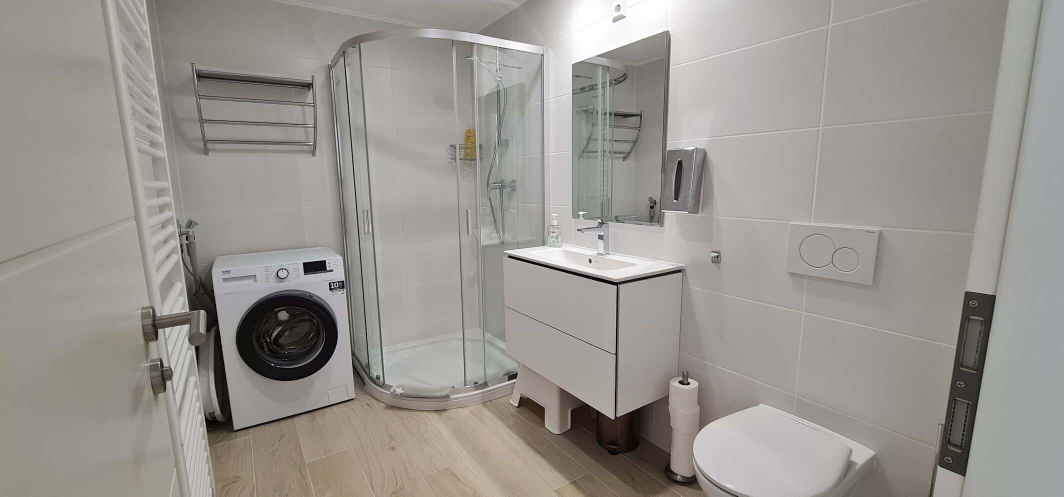 A modern bathroom with a glass shower enclosure, a built-in washing machine, a sink with a mirror, and a toilet.