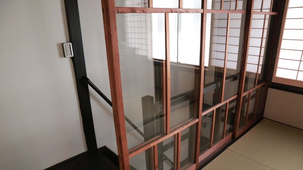 A room with tatami flooring, a sliding glass door with a wooden frame, and a white wall with a light switch. - Kyomachiya-Oyado Hana (Kyoto)