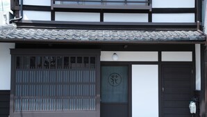 A traditional Japanese building with a sliding door, a tiled roof, and a dark wooden door with a circular emblem. - Kyomachiya-Oyado Hana (Kyoto)