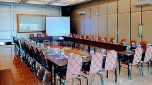 Un salón de conferencias con una larga mesa, sillas, una pantalla de proyector y una pantalla de presentación.
