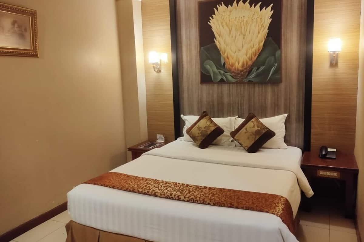 A hotel room with a large bed, a painting of a flower on the wall, and two bedside lamps.