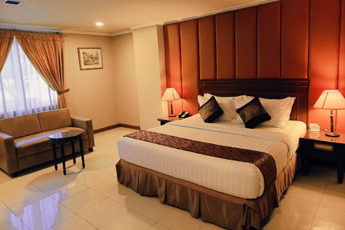A hotel room with a bed, a sofa, a small table, and a nightstand with lamps.