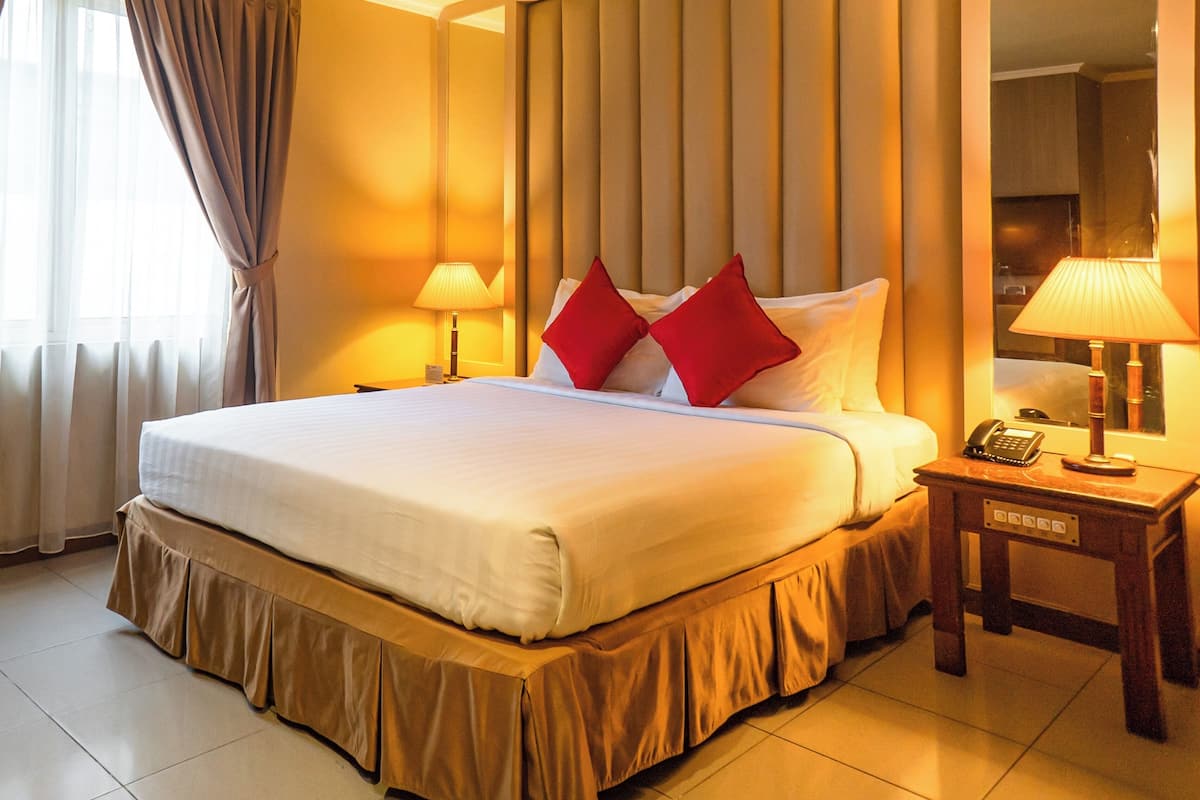 A hotel room with a large bed, two bedside lamps, a nightstand with a telephone, and a large mirror on the wall.