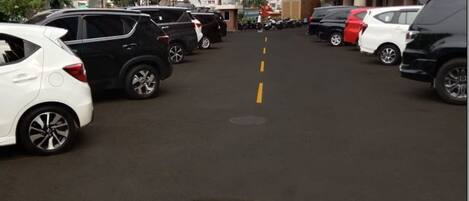 A parking lot with multiple cars parked in rows, a clear sky with scattered clouds, and palm trees lining the street.
