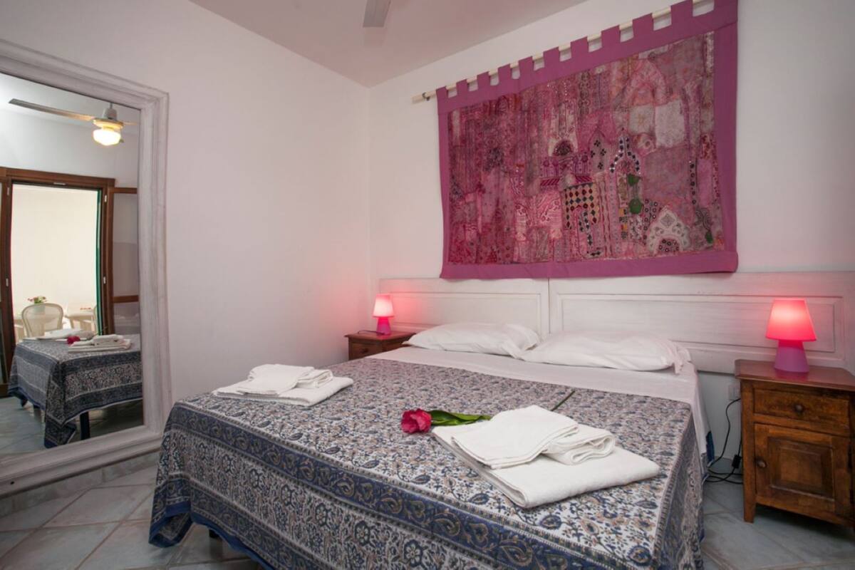 A hotel room with a large bed, two bedside tables, a mirror, and a decorative tapestry.