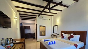 Quarto de hotel com cama de madeira, escrivaninha com chaleira e televisão na parede.