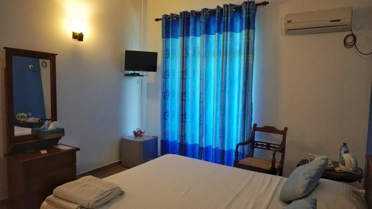 Een hotelkamer met een bed, een televisie, een bureau met stoel, en een raam met blauwe gordijnen.