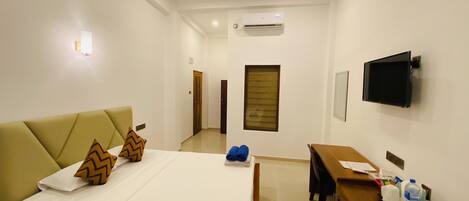 A hotel room with a bed, a desk, a TV, and an air conditioning unit.