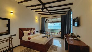 Quarto de hotel com cama, escrivaninha, televisão e varanda com vista para o mar.