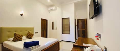 Habitación de hotel con cama, escritorio, televisor y baño visible a través de una puerta abierta.