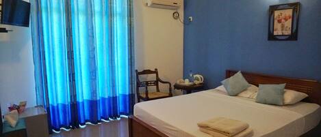 Una camera da letto con un letto, una sedia, un comodino, un condizionatore d'aria, una televisione e un quadro appeso al muro.