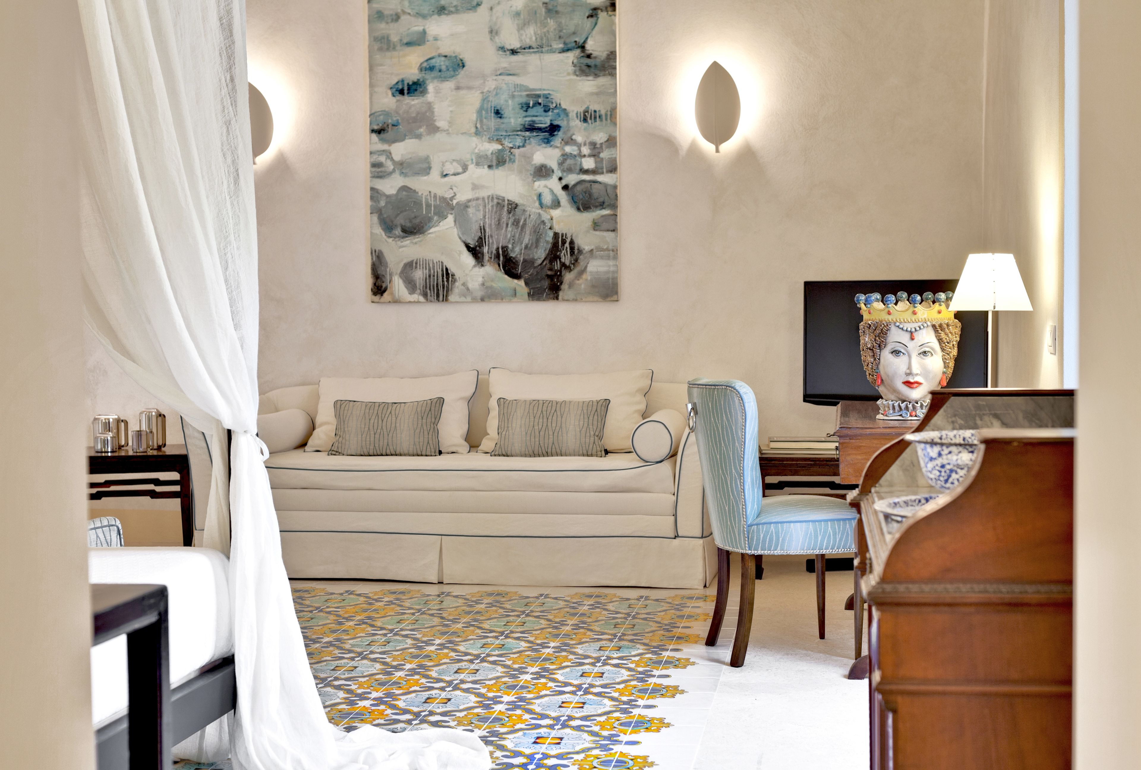 A room with a sofa, a chair, a bed with a canopy, a wall-mounted TV, and a decorative lamp.