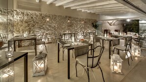 Un espace repas aux murs de pierre, avec des poutres en bois et des tables dressées pour le dîner.