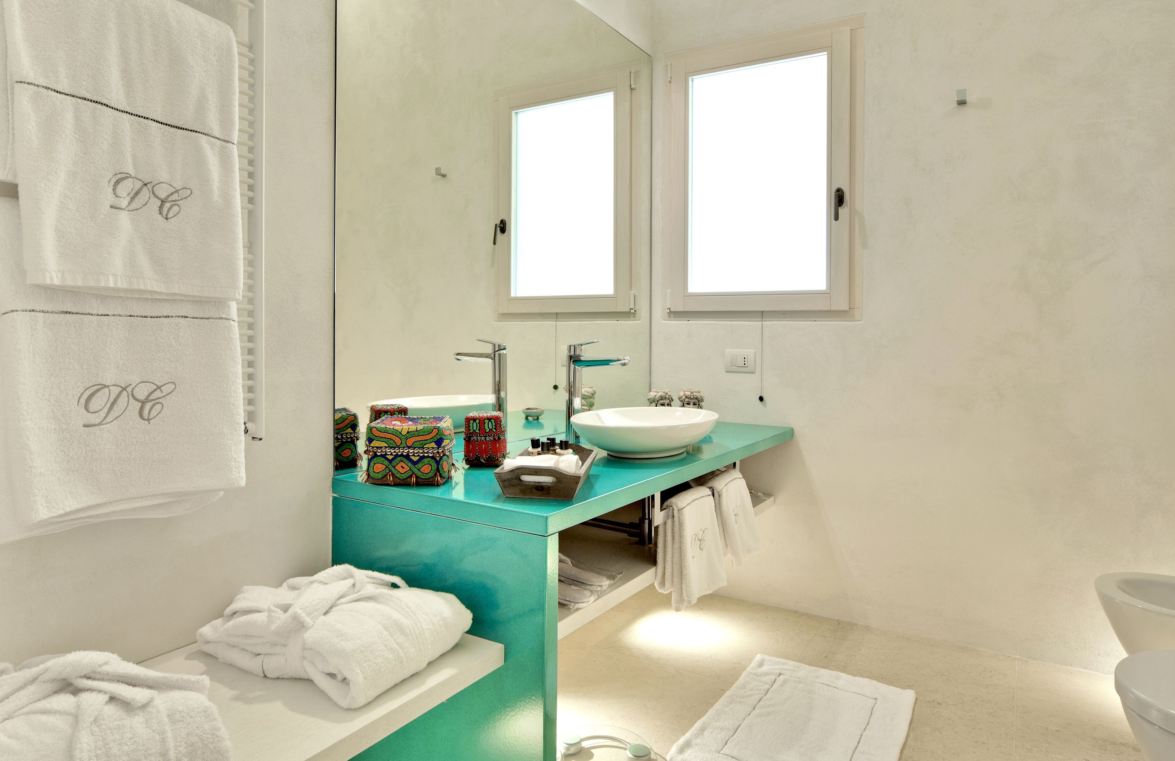 A modern bathroom with a teal vanity, white sink, and two mirrors. There are towels and toiletries on the counter.