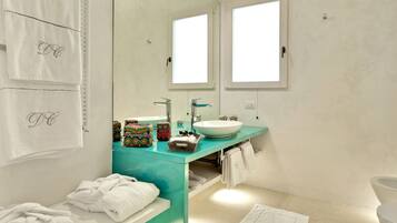 A modern bathroom with a teal vanity, white sink, and two mirrors. There are towels and toiletries on the counter.