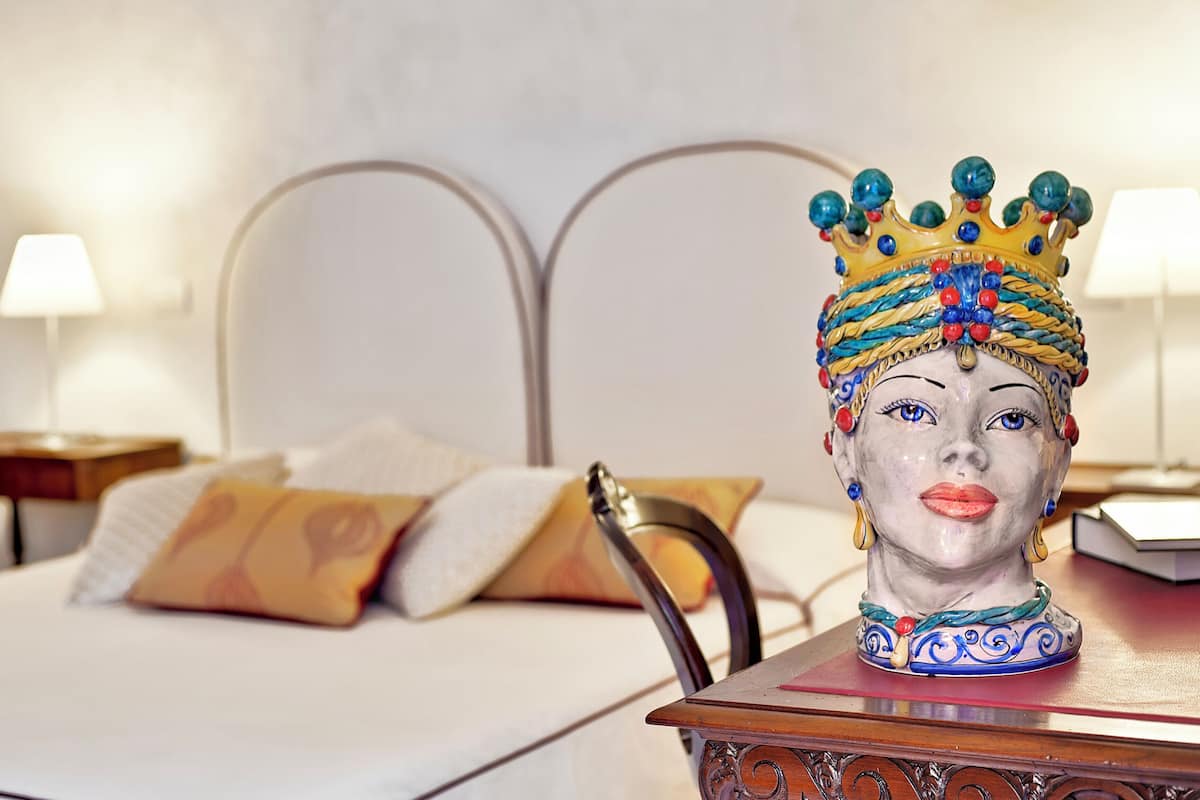 A bed with white linens and a decorative headpiece on a wooden nightstand.