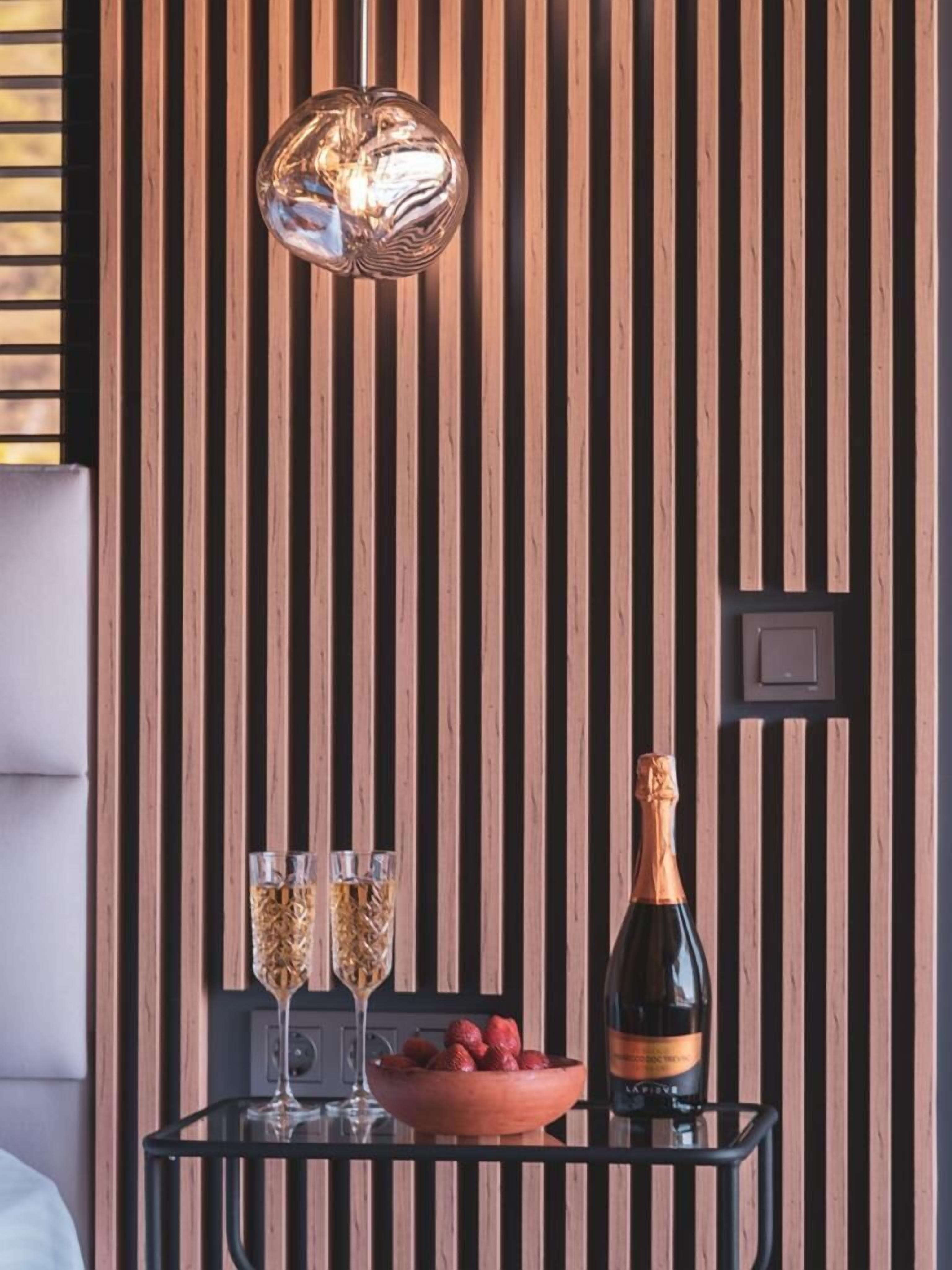 Un interior moderno con un panel de madera, una mesa de metal negro con una botella de champán, dos copas y un bol de fruta.