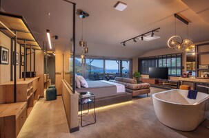 A modern living room with a large window, a sofa, a coffee table, and a unique bathtub.