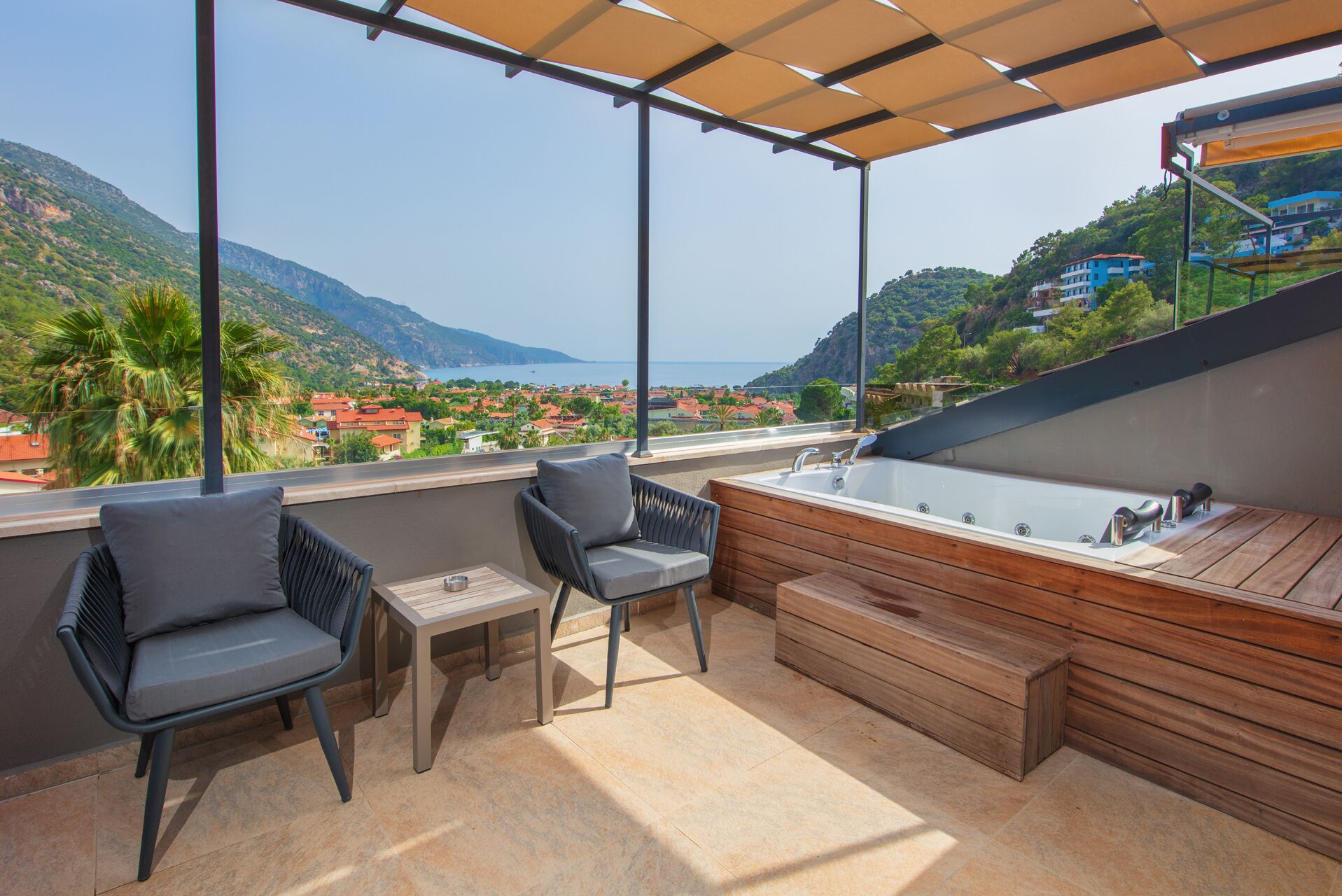 A balcony with a wooden bench, two chairs, a small table, and a bathtub.