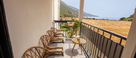 A balcony with wicker furniture, a small table, and a view of a beach and mountains.