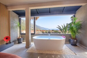 A modern bathroom with a freestanding bathtub, large windows, and potted plants.