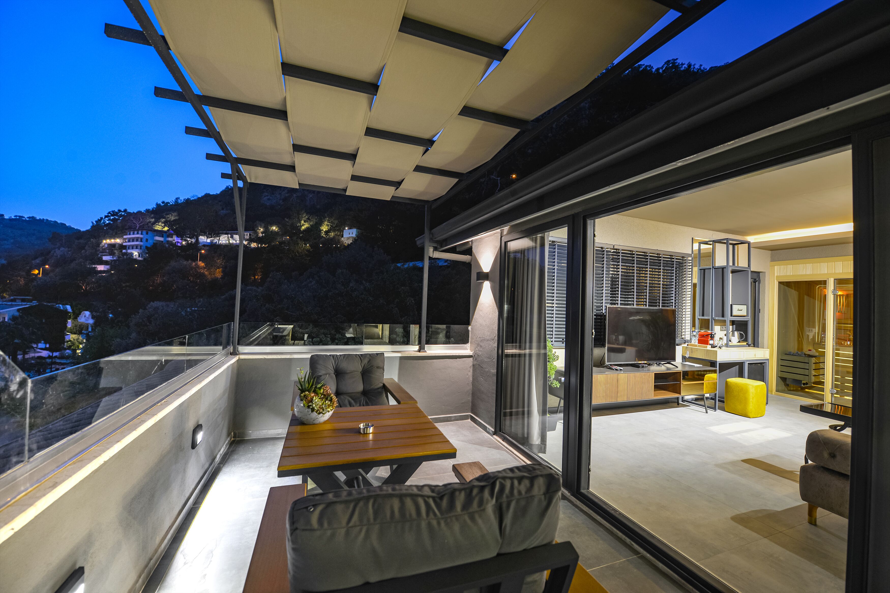 Un balcón moderno con comedor, sofá y cocina visible a través de puertas de vidrio.