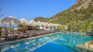 Zona de piscina con sillas de descanso y sombrillas, rodeada de un paisaje montañoso.