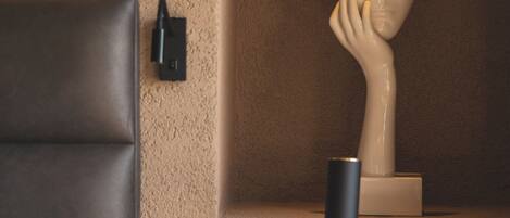 Un dormitorio con una mesita de noche de madera, una lámpara, un busto y un cuadro de interruptores en la pared.