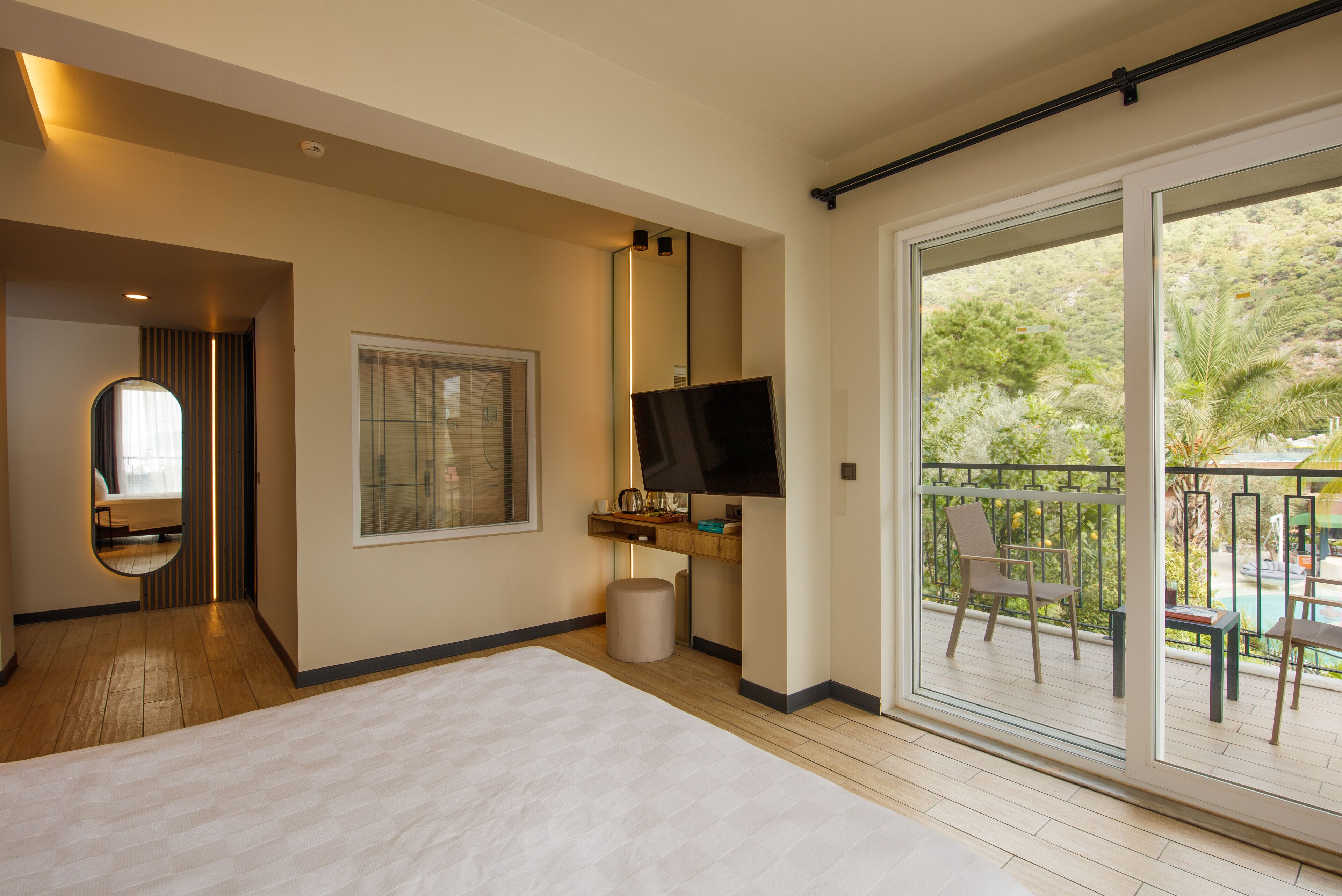 Habitación de hotel con una cama grande, televisión, ventana y balcón con mobiliario exterior.