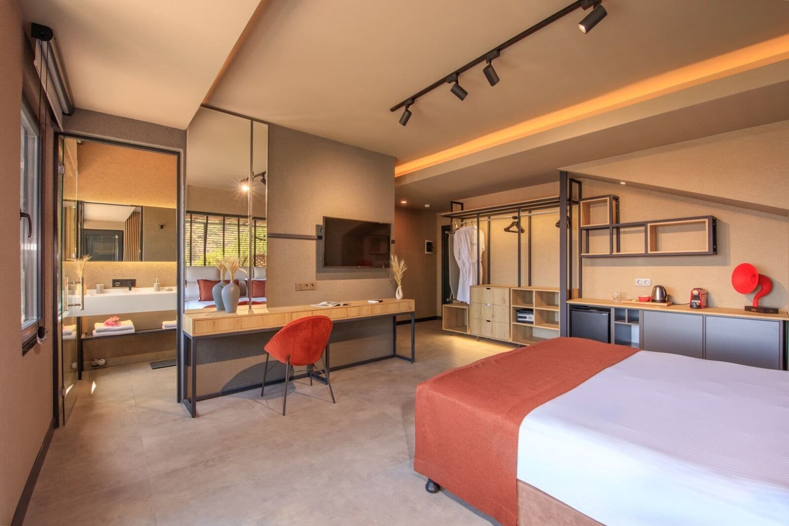 Una habitación de hotel moderna con una cama grande, un escritorio con una silla, un vestidor y un baño con un espejo amplio.