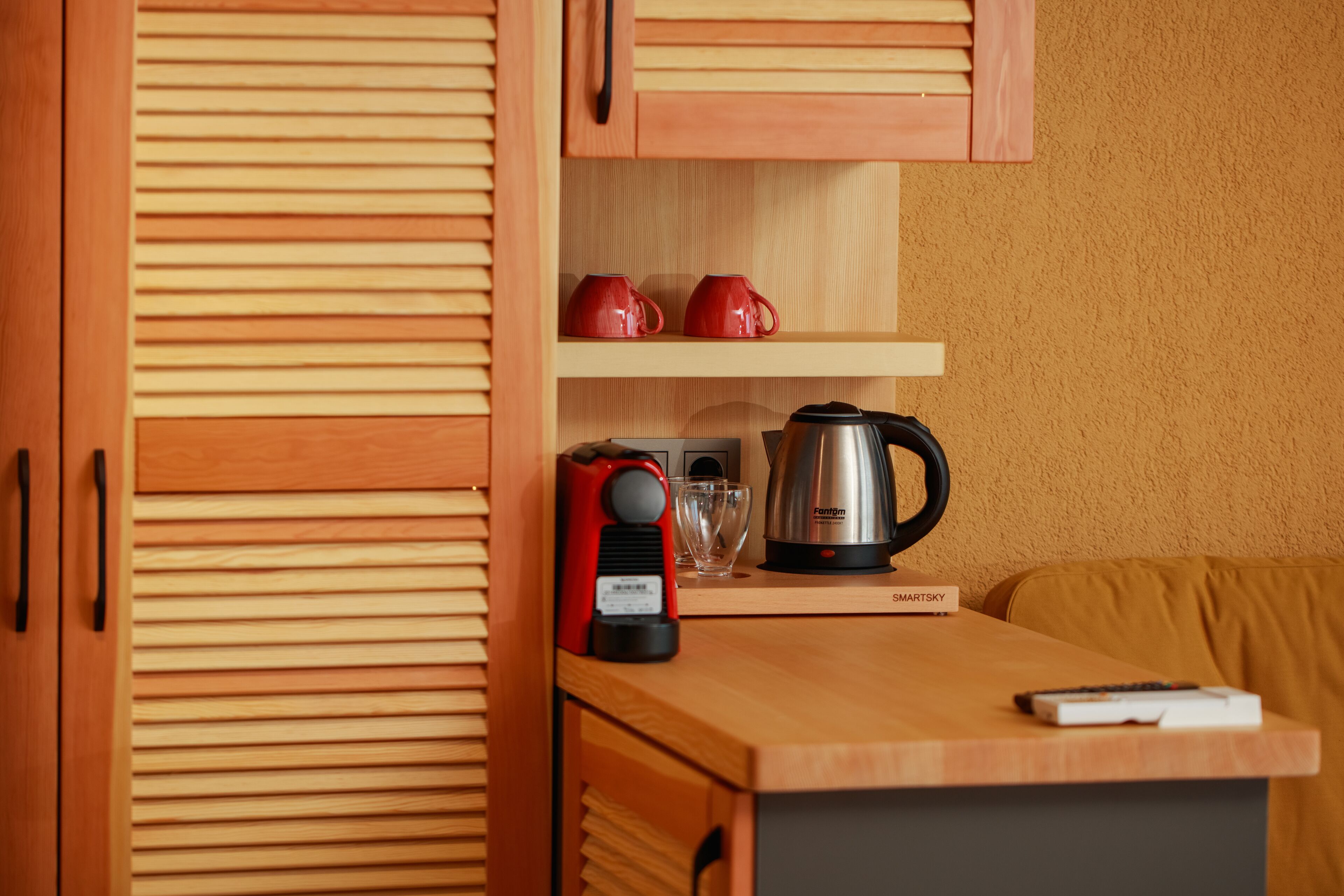 A compact kitchen with wooden cabinets, a coffee maker, and a remote control on the counter.