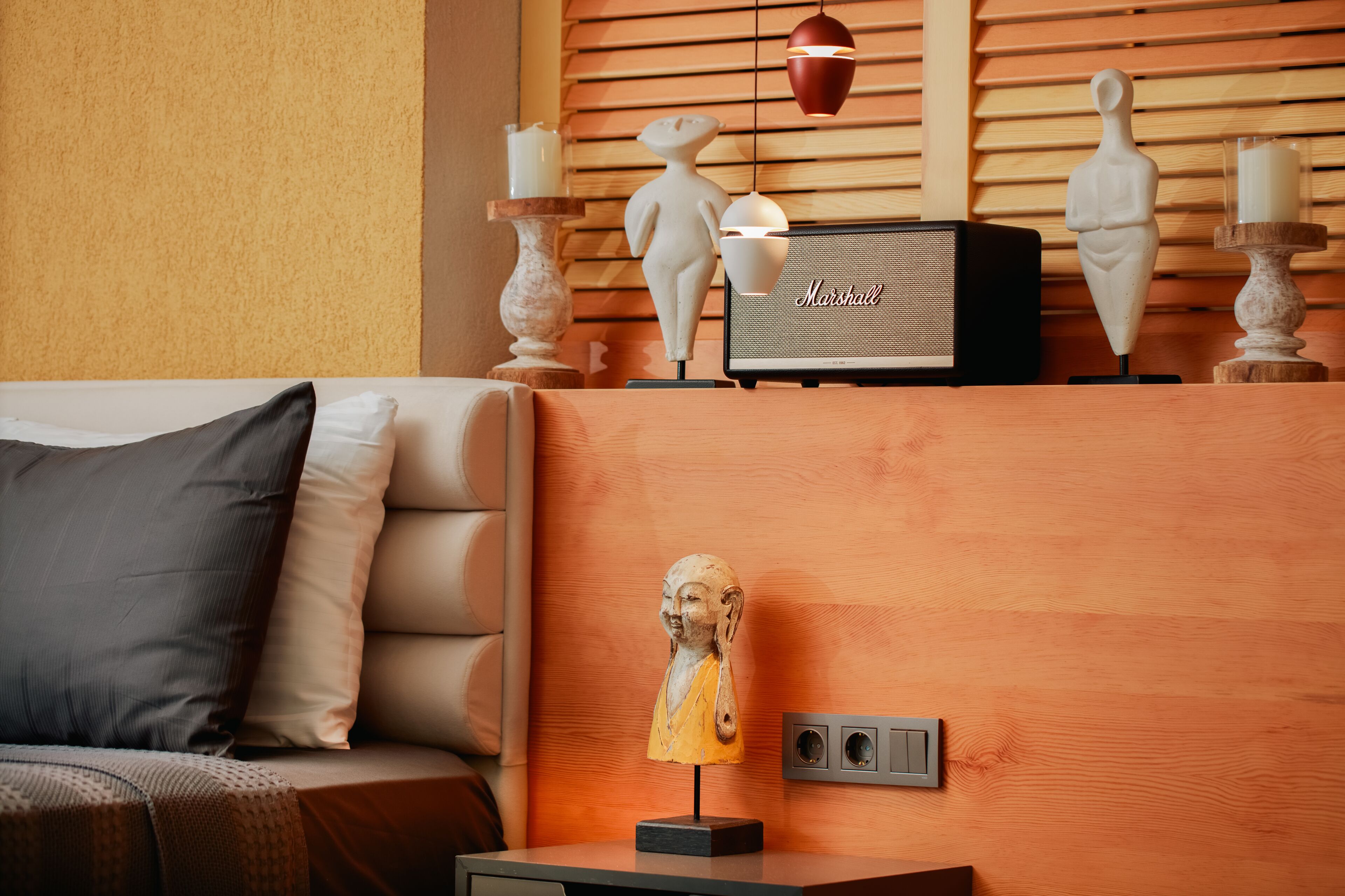 A modern living room with a sofa, a small table with a sculpture, a Marshall speaker, and decorative items on a wooden wall.