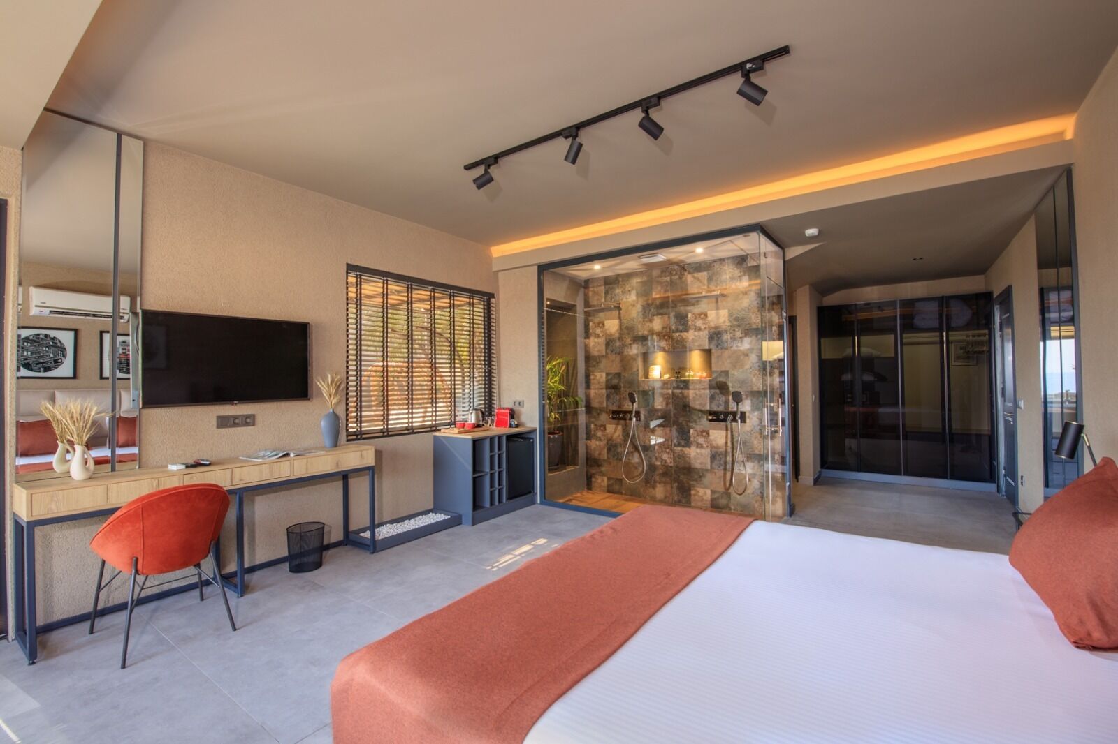 A modern hotel room with a desk, chair, bed, and a shower area.