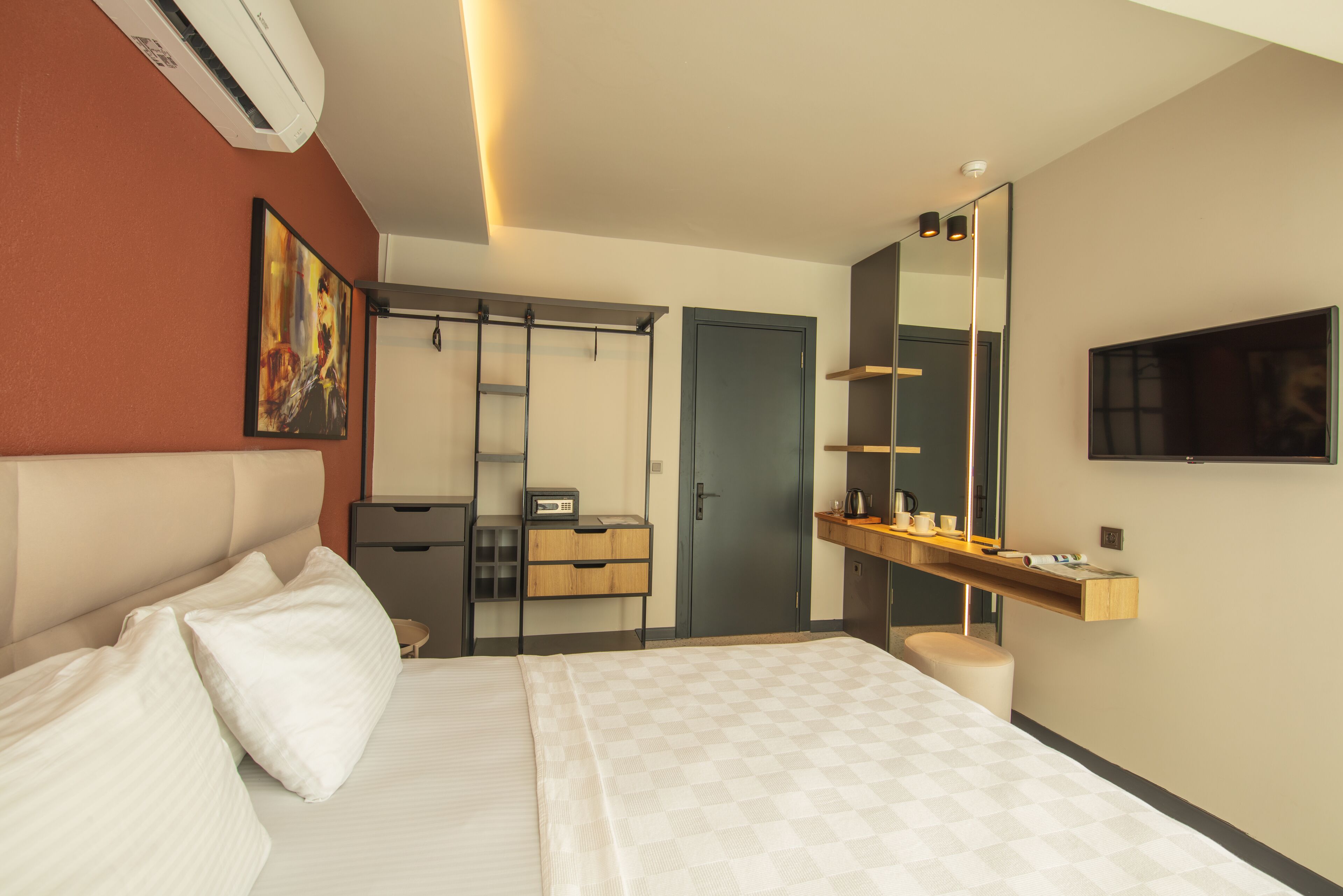 A modern hotel room with a large bed, a wardrobe, a desk with a chair, a mirror, and a TV mounted on the wall.
